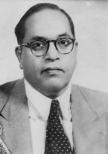 Black-and-white photograph of B. R. Ambedkar, wearing a suit and glasses, seated at a desk in Delhi in 1948.