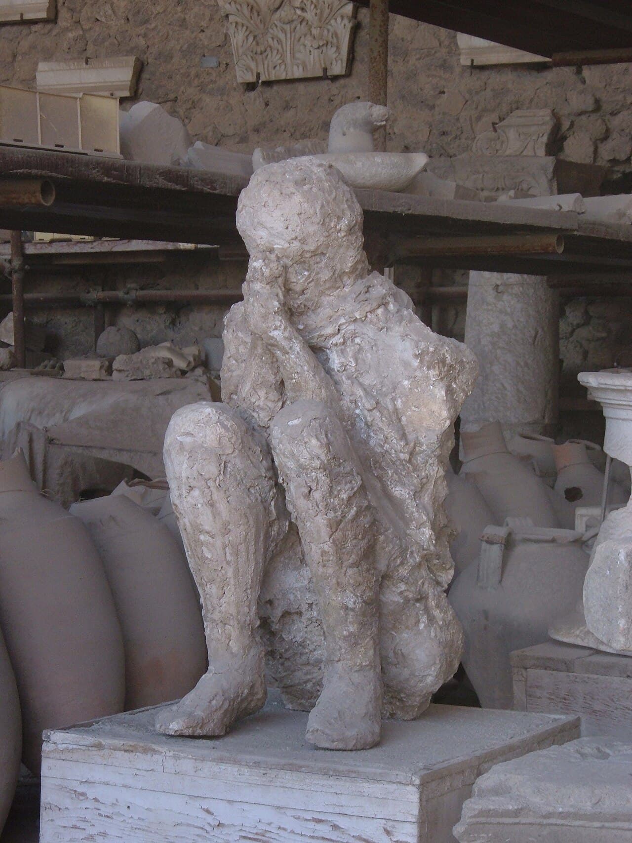 A plaster cast of a Pompeii victim lying curled on the ground, showing the folds of clothing and body position preserved in the ash.