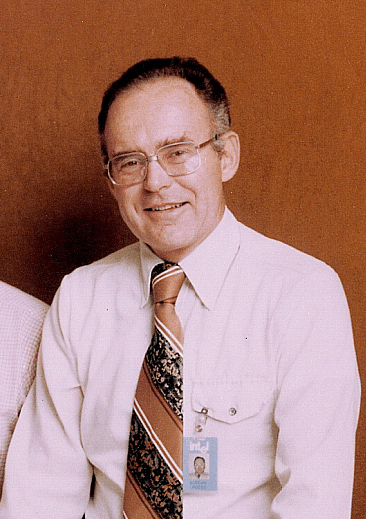 A black-and-white photo of Gordon Moore, a man in glasses and a suit, from the late 1970s.