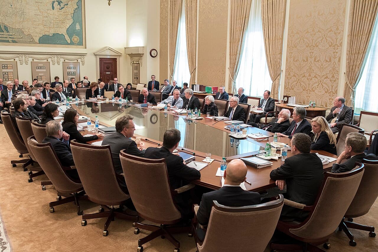 Members of the Federal Open Market Committee seated around a large table in a formal room at the Federal Reserve in Washington.