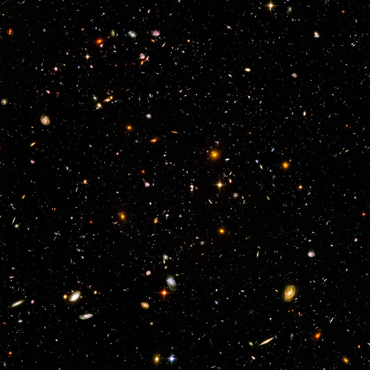 The Hubble Ultra-Deep Field: thousands of small galaxies of varied shapes and colors against a black background dotted with points of light.