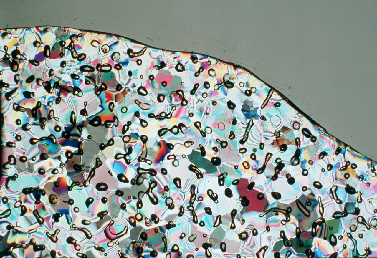 A thin slice of Antarctic ice lit with polarised light, showing colourful crystals dotted with hundreds of tiny round air bubbles.