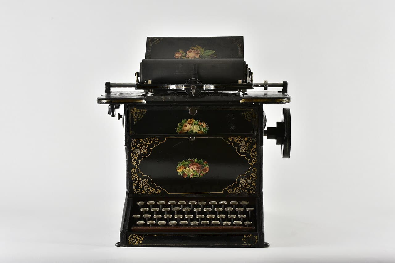 An ornate black Sholes and Glidden typewriter from 1873, decorated with painted flowers, with round keys arranged in four rows.