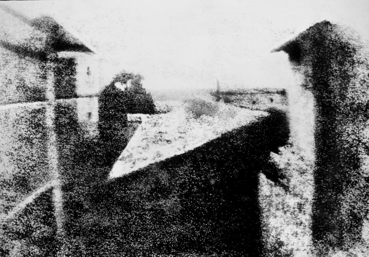 A faint, blurry, grainy sepia-toned image of rooftops and a courtyard, barely distinguishable, on an aged pewter plate.