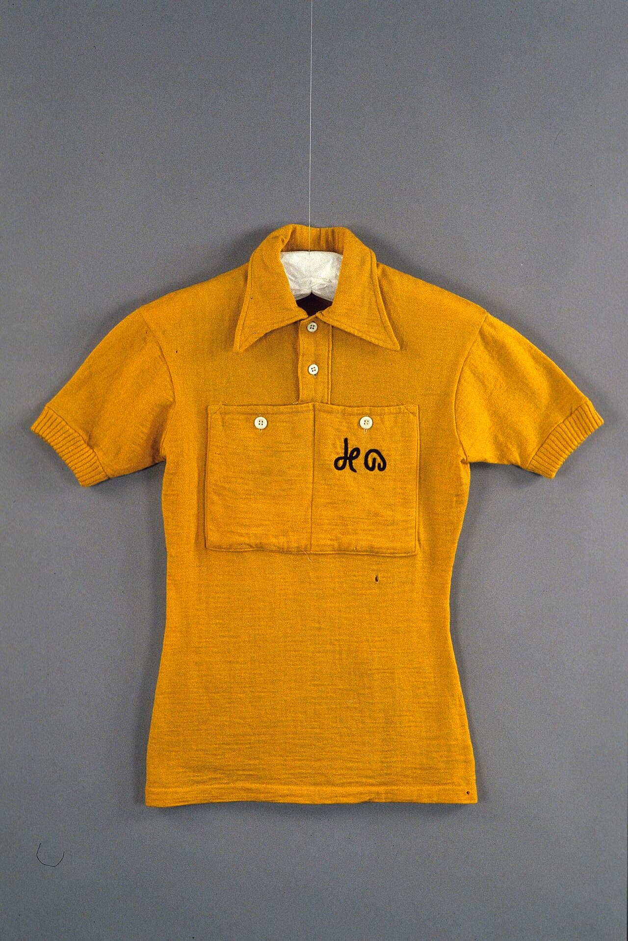 A woollen yellow cycling jersey from the 1954 Tour de France, worn by Louison Bobet, photographed flat in a museum collection