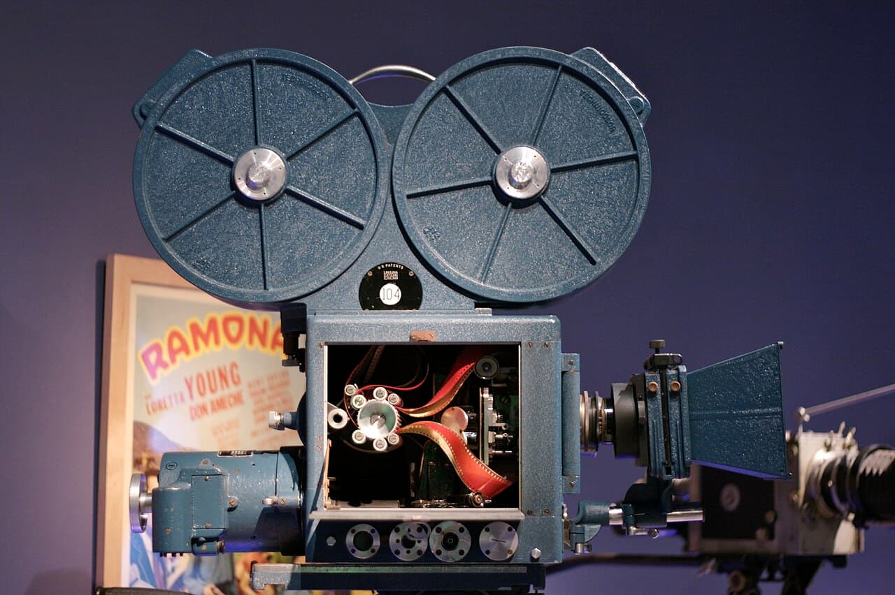 A large, boxy 1930s film camera with a lens on the front and film magazines on top, displayed in a museum.