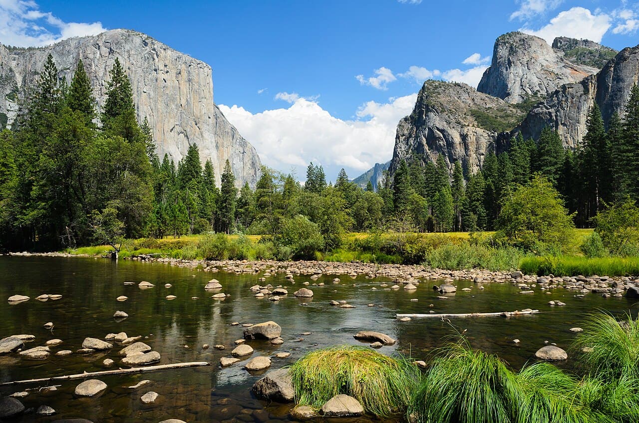Yosemite Valley seen from Valley View, with sheer granite walls rising on both sides of a flat, forested valley floor and a river in the foreground.